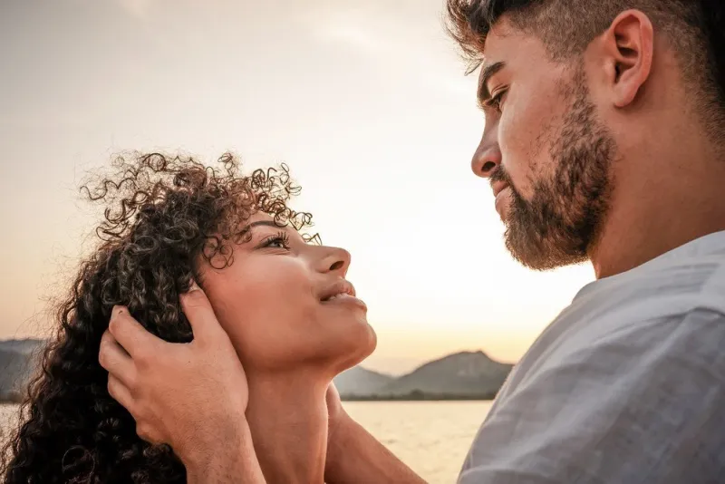 close up portrait of young mixed race couple in love looking in eyes each other in sunset color mood macho dominant handsome man holding face of his worshiping submissive woman with intense gaze