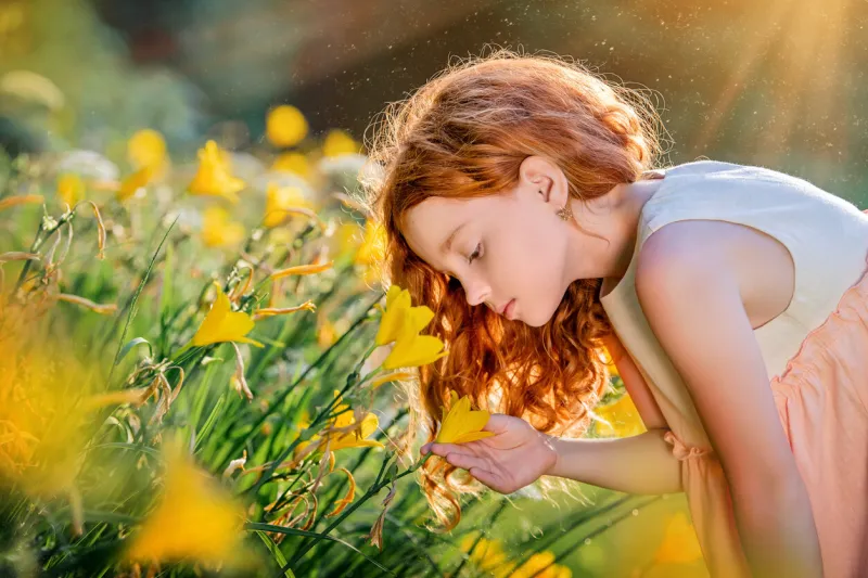 red-haired girl smells flowers in a sunny blooming garden in summer