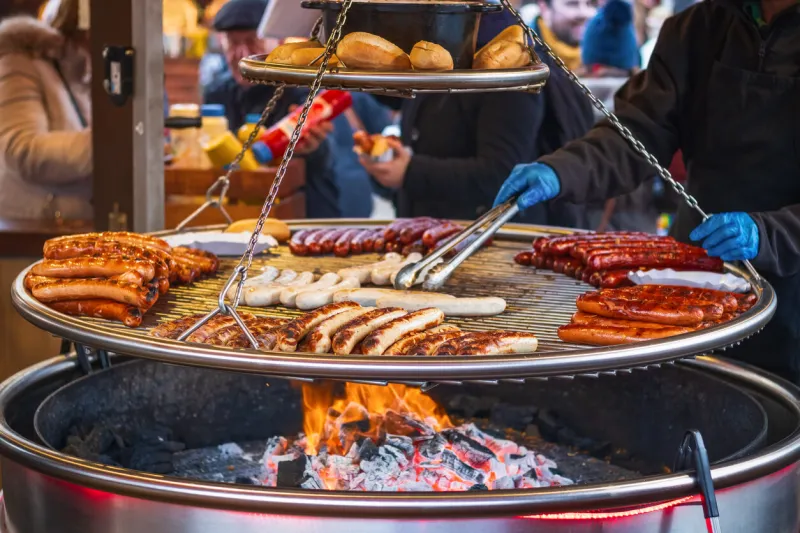 grilling sausages on barbecue grill at a food stall of christmas market winter wonderland in london