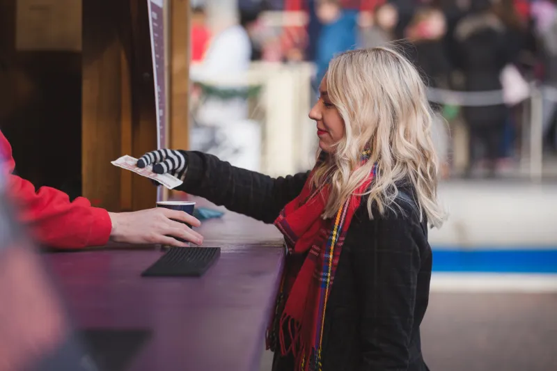 a young woman purchases a hot drink from a vendor to keep warm while attending the edinburgh christmas market