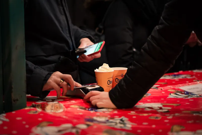 haarlem, netherlands - 9 dec 2018  person holding phone pays with a contact debit or credit card for two hot chocolates at a holiday christmas street market bright red, festive tablecloth