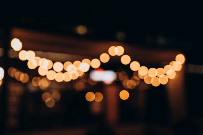 decorative outdoor string lights at night time, defocused background, night city life backdrop, party time with yellow bokeh balls