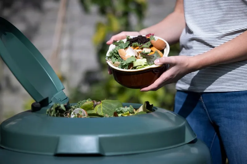 close up of woman emptying food waste into garden composter at home