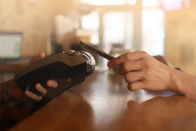 macro unknown hand giving terminal to visitor for mobile phone payment indoor client hand paying bill with smartphone in blurred background cropped shot hands making contactless transaction inside