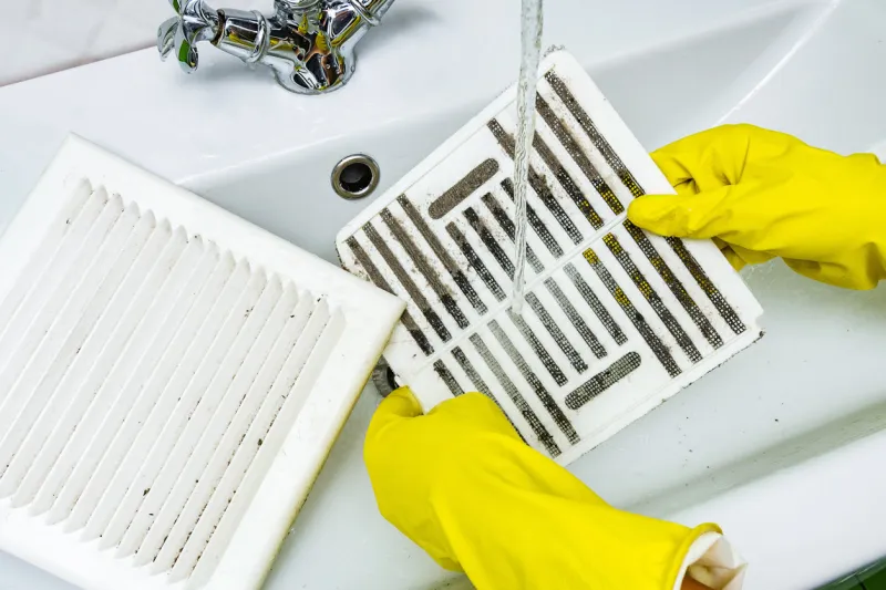 person in a protective rubber glove washes in the sink air filter of the ventilation return duct blocked by dust and debris cleaning service