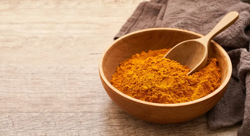 close up a pile of ground turmeric powder or curcumin powder in wood plate and scoop on wooden table background turmeric or curcumin powder