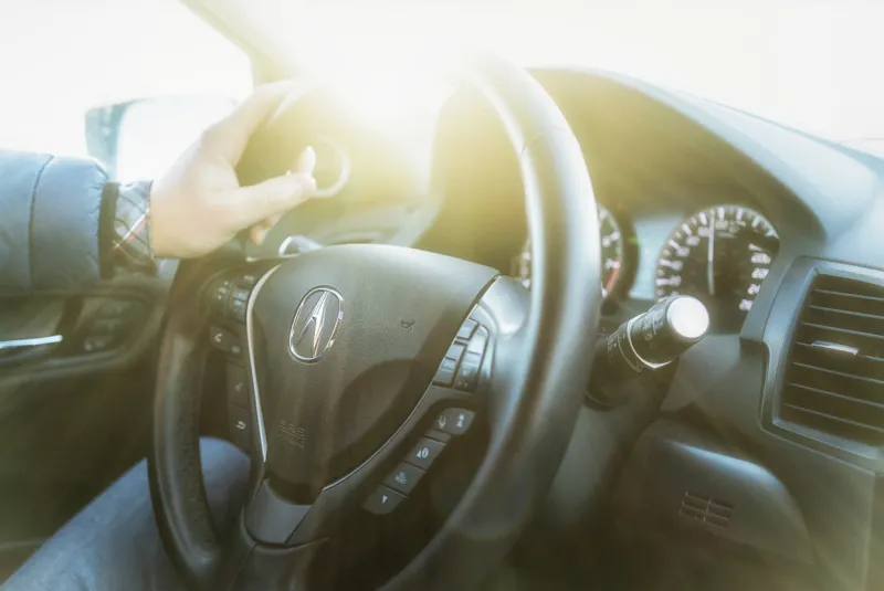 closeup of a acura (rdx 2017) car steering wheel lots of sunlight around acura canada one hand on the steering wheel driving a car