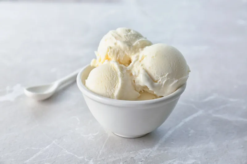 bowl with tasty vanilla ice cream on light background
