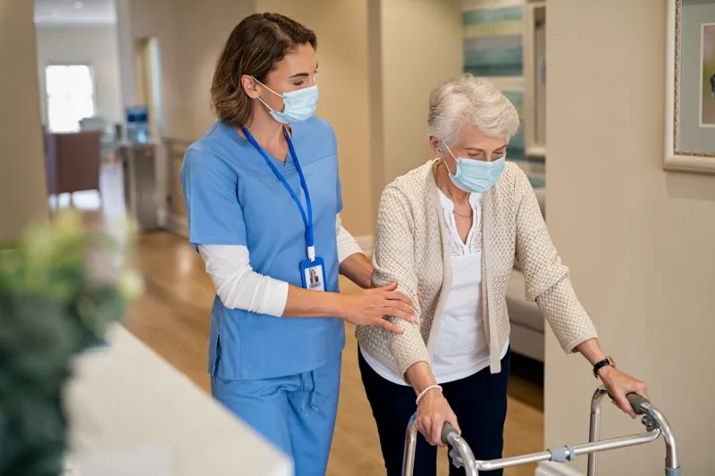 nurse helping senior woman walk at nursing home