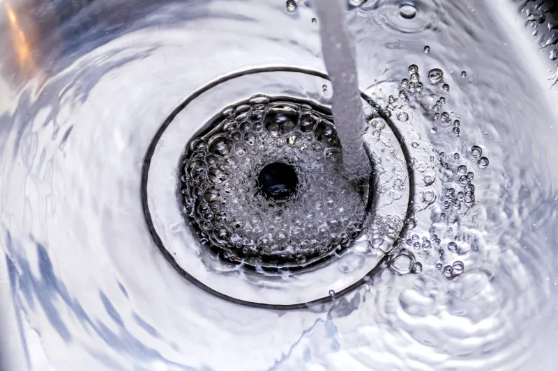 a stream of clean water flows into the stainless steel sink sink plug hole close up macro