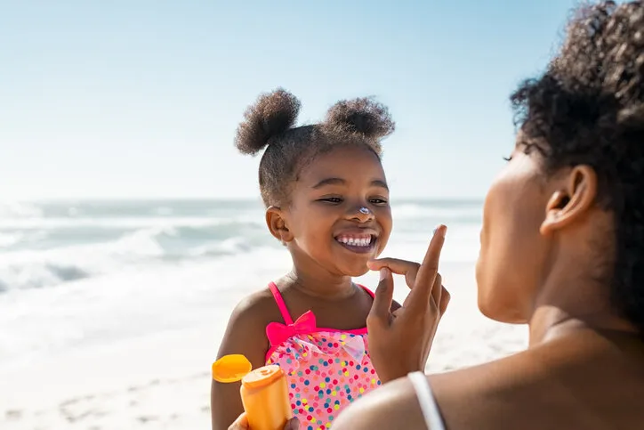 young mother applying protective sunscreen on daughter nose at beach with copy space black woman hand putting sun lotion on female child face african american cute little girl with sunblock cream at seaside