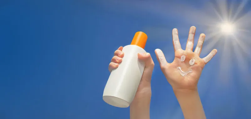 positive symbol drawing by sunscreen on open hand another hand holding a bottle of sun cream blue sky, beams of sun background protection of sun copy space
