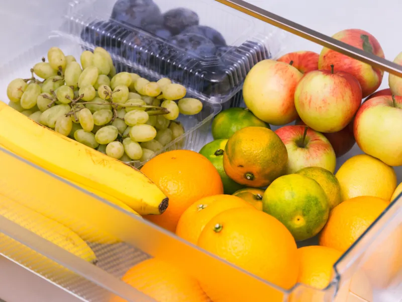 a fridge drawer full of fruits (oranges, tangerines, grapes, bananas, apples, plums)