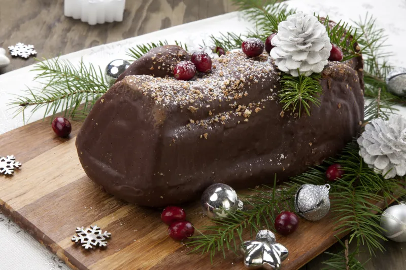 traditional christmas chocolate yule log cake with cranberry, christmas ornamets, and decorations