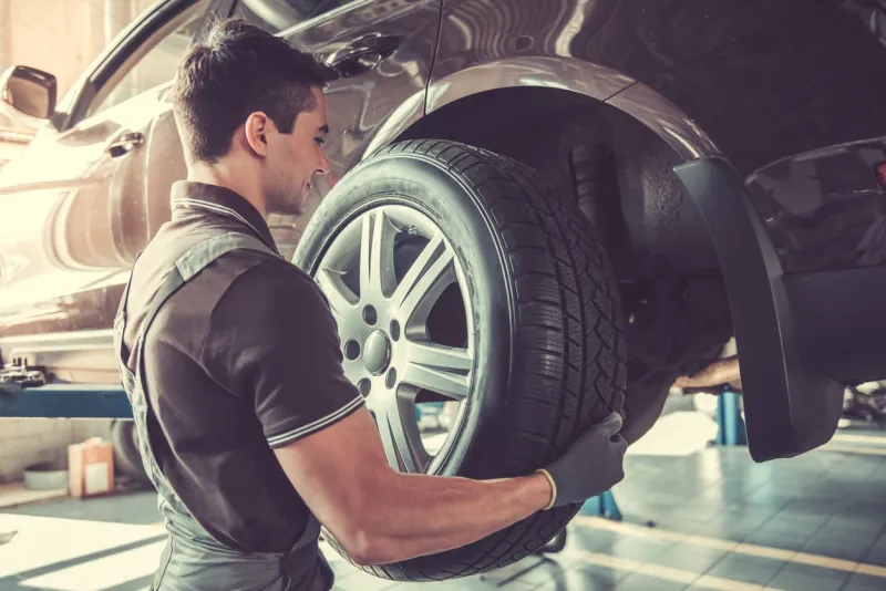 handsome young auto mechanic in uniform is changing a tire while working in auto service