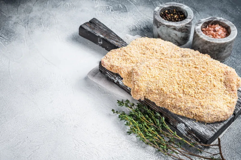 wiener raw schnitzel in breadcrumbs on wooden board white background top view copy space