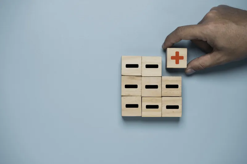 hand move red plus sign move out from black minus sign which print screen on wooden cube on blue background for positive thinking and mindset concept