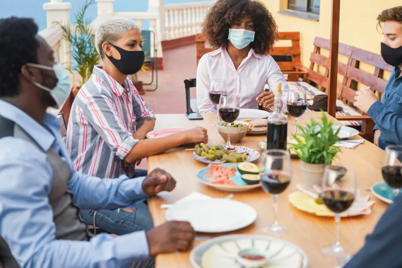 young multiracial people eating and drinking together while wearing face protective masks - focus on black girl