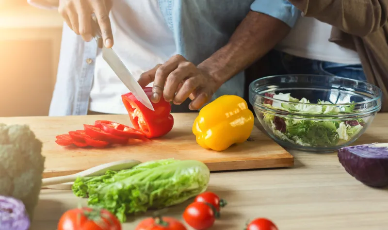 black man cutting vegetables for healthy vegetarian salad in kitchen, closeup