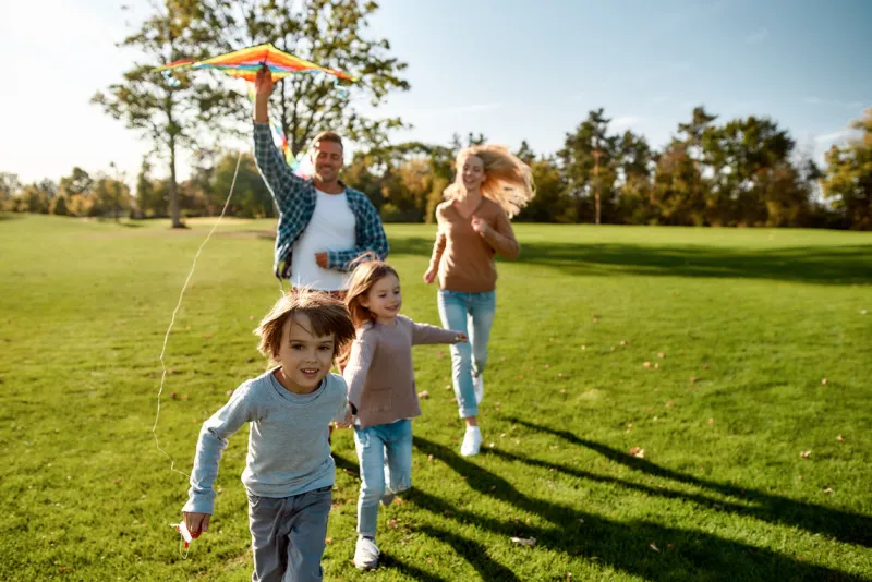 portrait of cheerful parents with two kids running with kite in the park on a sunny day family, kids and nature concept horizontal shot