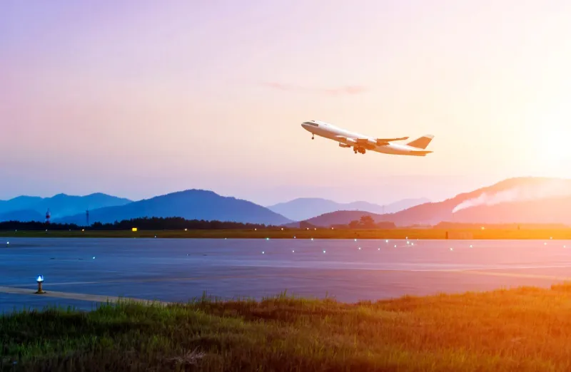 passenger plane fly up over take-off runway from airport at sunset