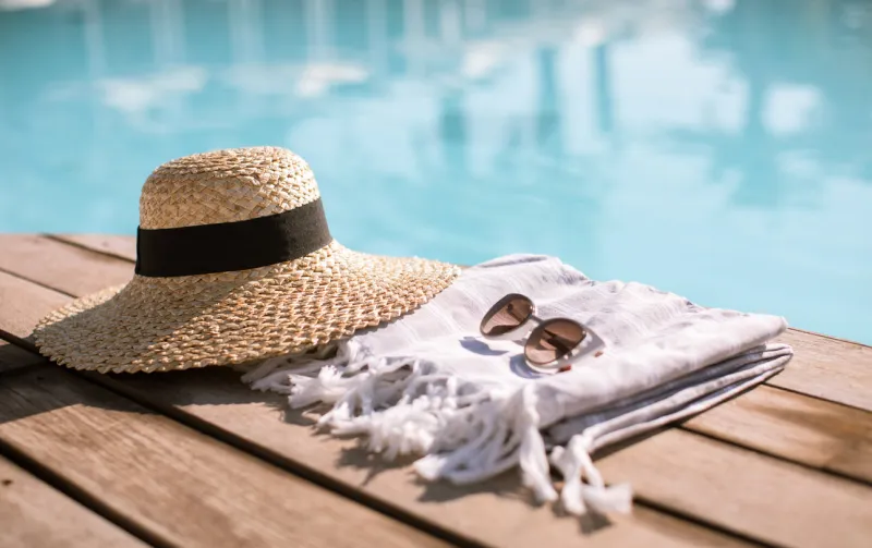 sunglasses and straw hat on the wooden floor at the pool summer vacation fashion concept
