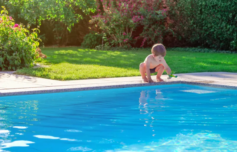 little happy boy sitting on side of swimming pool in garden playing with his toy having fun summertime summer holidays