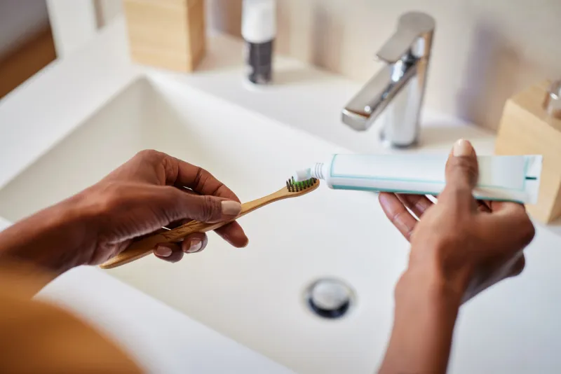 black woman hand squeezing whitening paste on wooden toothbrush, taking care about mouth hygiene close up of female hands applying toothpaste on ecological bamboo tooth brush, plastic free concept oral hygiene and environmental responsibility concept