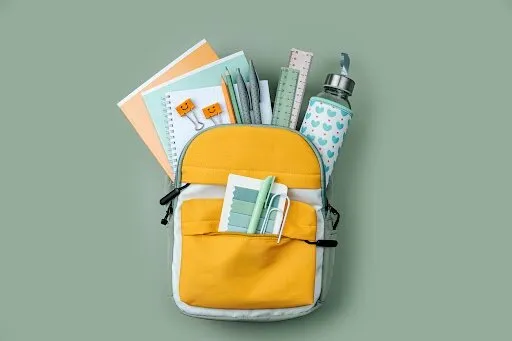 opened school backpack with stationery on green background concept back to school school supplies