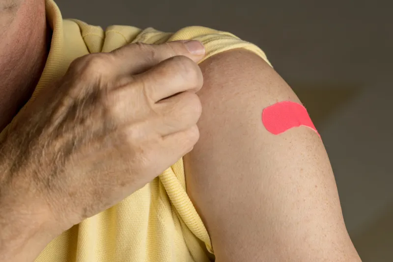 senior caucasian man holding up shirt sleeve to show the sticking plaster after a flu jab in shoulder