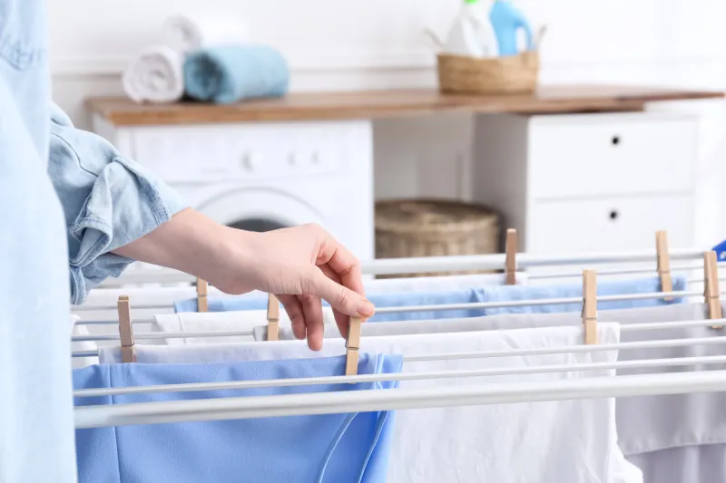 woman hanging clean laundry on drying rack in bathroom, closeup