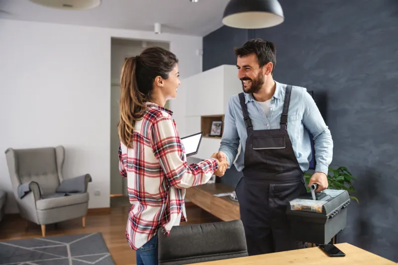 happy woman shaking hands with repairman home interior