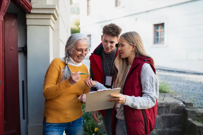 young door to door volunteers talking to senior woman and taking a survey at her front door