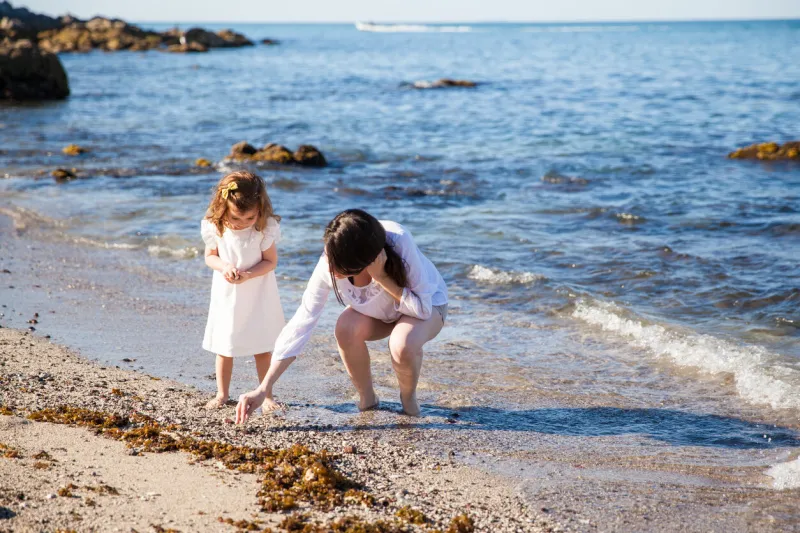 young mother and her daughter walking down the beach and looking for sea shells