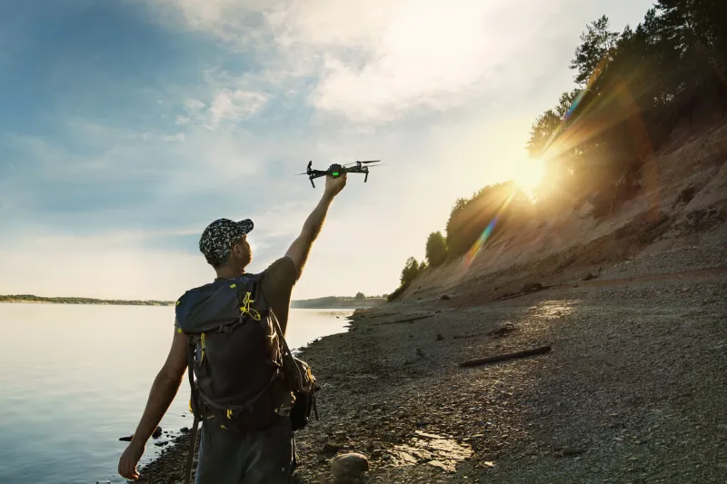 male tourist launching drone from hand in beautiful sunset in woodland