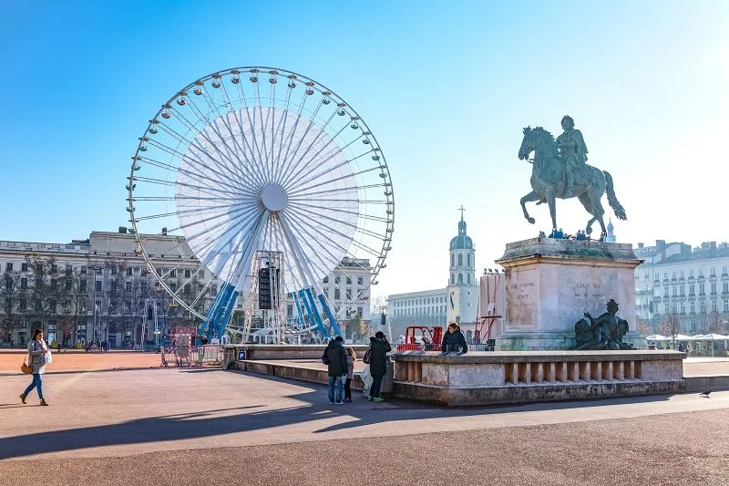 lyon, france - december 8, 2016  bellecour square, young people under the equestrian monument of king louis xiv with the big ferris wheel in the background