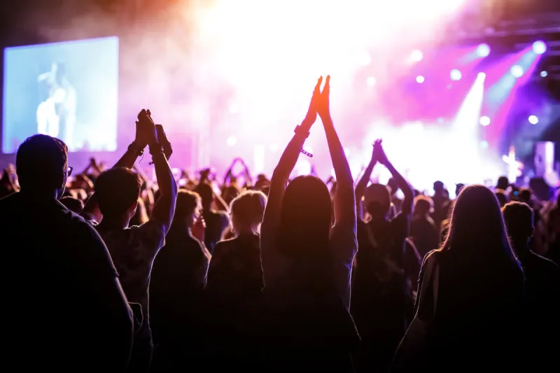 people with raised hands, silhouettes of concert crowd in front of bright stage lights