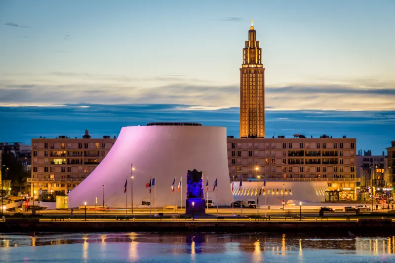 le havre, france - june 9, 2021  the volcan cultural center and the oscar niemeyer public library with the war memorial in the foreground and the bell tower of st joseph's church at nightfall
