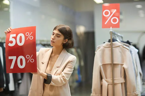 waist up portrait of beautiful woman hanging red sale signs on window display in clothes store, copy space