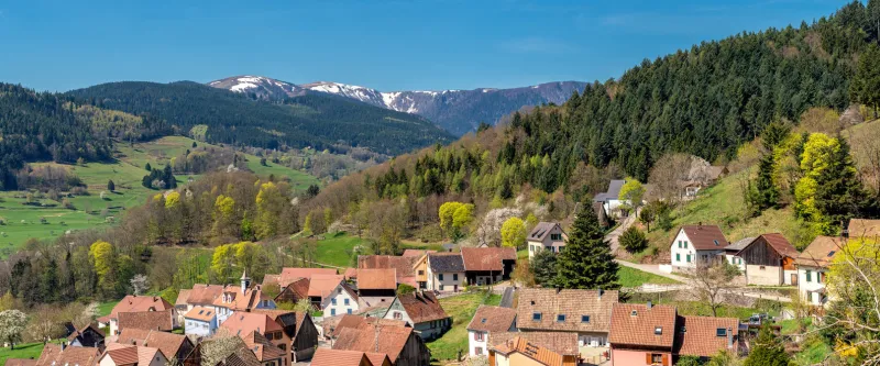 panoramic view of a small village in the vosges with snow covered mountains in the background