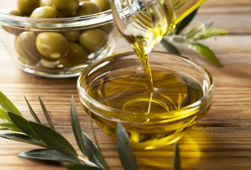 the moment olive oil is poured into a glass bowl set against a wooden background