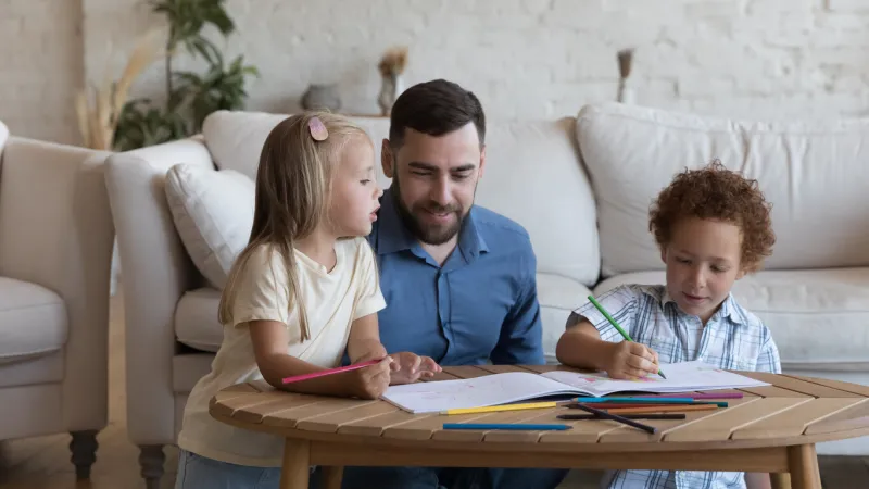 happy dad enjoying creative leisure time with two sibling kids, watching children drawing in colorful pencils in album, talking, helping, giving support family playtime, fatherhood concept banner