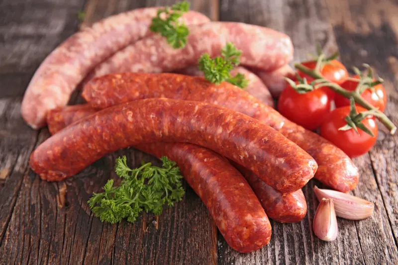 pile of raw sausages with herbs and spices on a wooden table