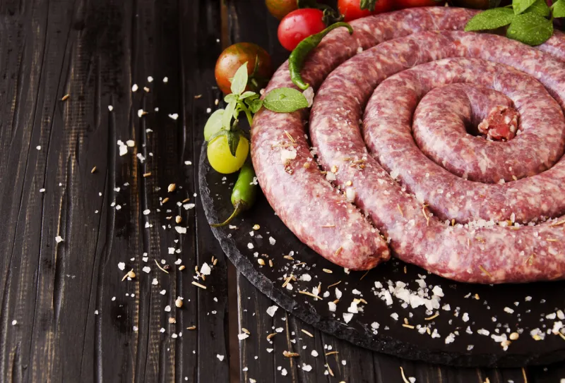 raw beef sausages with rosemary and spices on a wooden table, south african boerewors