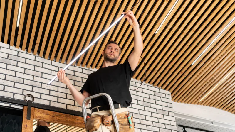 an electrician installs low voltage led lamps in a pine plank ceiling rent-a-gent provides service for the repair of electrical wiring and replacement of lamps builder assembles loft ceiling