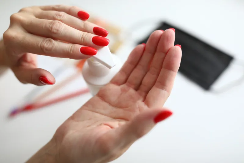 close-up of female pressing moisturizing lotion on hand woman smoothing hands beautiful bright red manicure taking care of skin beauty and cosmetics concept