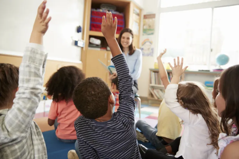 elementary school kids raising hands to teacher, back view