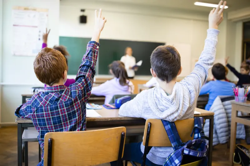 schoolchildren at classroom with raised hands answering teacher's question