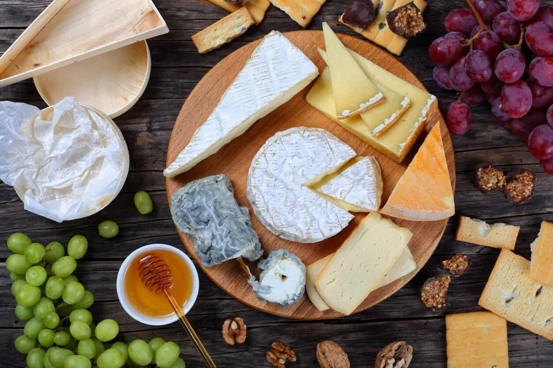 set of authentic french cheese plate served with grapes, honey, homemade chocolate sweets and nuts on wooden round tray on dark wooden background, view from above