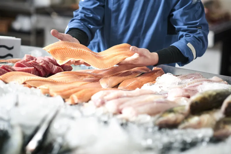 a young male shop assistant in a fishshop saling fresh fish